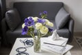 Bouquet of white ranunculus and blue anemone in the vase on a white coffee table near the grey sofa with plaid. The books and Royalty Free Stock Photo