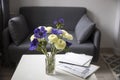 Bouquet of white ranunculus and blue anemone in the vase on a white coffee table near sofa with plaid. The books and journal Royalty Free Stock Photo