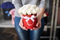 A bouquet of white rose buds in a round red box with a white ribbon in the careful hands of a girl.