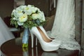 Bouquet of white roses and elegant wedding shoes on wooden table Royalty Free Stock Photo