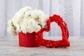 A bouquet of white roses in a red box and a photo frame a heart made of red rattan, close-up. Royalty Free Stock Photo
