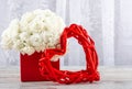 A bouquet of white roses in a red box and a photo frame a heart made of red rattan, close-up. Royalty Free Stock Photo