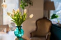 A bouquet of white tulips in a blue green glass vase in bright morning sun. Modern interior design, fresh spring flowers.