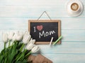 A bouquet of white tulips with chalk board, cup of coffee, love note and envelopes on blue wooden boards . Mother`s day