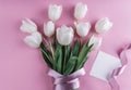 Bouquet of white tulips flowers and sheet of paper over light pink background.