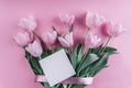 Bouquet of white tulips flowers and sheet of paper over light pink background. Greeting card or wedding invitation.