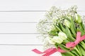 Bouquet of white tulips and gypsophila decorated with red ribbon on white wooden background. Top view Royalty Free Stock Photo