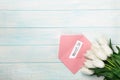 A bouquet of white tulips with a love note and color envelope on blue wooden boards . Mother`s day