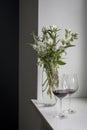 A bouquet of white veronica with white bells in tall narrow vase on a grey table on the white background. red wine in tall glass