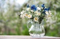 A bouquet of wild flowers of chamomiles and cornflowers in a glass vase on a wooden table in the garden Royalty Free Stock Photo