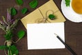 Bouquet of wild flowers, envelope with pencil and cup of tea on wooden background