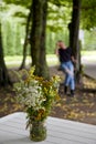 A bouquet of wild flowers in a glass jar against the background of a blurred silhouette of a woman on a swing Royalty Free Stock Photo