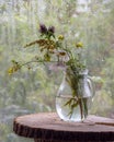 A bouquet of wild flowers in a glass jug on the background of a window with rain drops