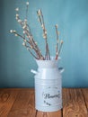 A bouquet of willow in a blue tall planter stands on a wooden table