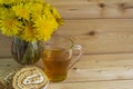 A bunch of yellow dandelions. A glass of tea in a glass mug. Two slices of honey roll with cream. Royalty Free Stock Photo
