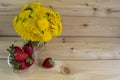 A bouquet of yellow dandelions on a warm wooden background. red strawberries in a glass vase. Royalty Free Stock Photo