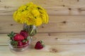 A bouquet of yellow dandelions on a warm wooden background. red strawberries in a glass vase. Royalty Free Stock Photo