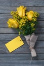 Bouquet of yellow flowers with blank paper card as tag for name logo or greetings on wooden background Royalty Free Stock Photo