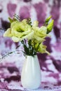 Bouquet of yellow-green lisianthus flower in white vase on violet background
