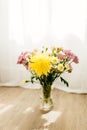 A bouquet of yellow and pink asters and gerbers in a glass vase against the backdrop of a window with rays of sun Royalty Free Stock Photo