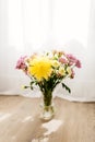 A bouquet of yellow and pink asters and gerbers in a glass vase against the backdrop of a window with rays of sun Royalty Free Stock Photo