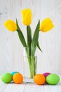 Bouquet of yellow tulips and colorful Easter eggs on a light wooden background. Paschal greeting card with spring flowers