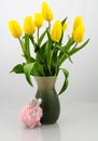 Bouquet of yellow tulips in a pleasing green vase isolated on a pale background. Pink bunny accents the base of the vase. Royalty Free Stock Photo