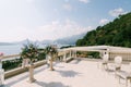 Bouquets of flowers in front of antique chairs stand on a terrace overlooking the sea and mountains