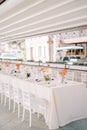 Bouquets of flowers stand on a festive long table under a canopy near the house