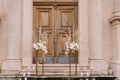 Bouquets of flowers stand on golden plinths in front of a wooden door of the church