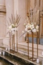 Bouquets of flowers stand on golden plinths on the steps in front of a wooden door