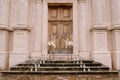 Bouquets of flowers stand on golden plinths on the wet steps in front of a wooden door of the church