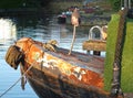 Bow of an old rusty iron canal boat with an old Buddha head moored with ropes on a jetty with reflections in dark water Royalty Free Stock Photo