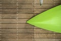 Bow of overturned green kayak laying on a natural wood dock with part of a chrome handrail at side