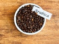 Bowl with Arabica coffee beans on wooden background