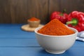 Bowl with aromatic paprika powder and fresh bell peppers on blue wooden table. Space for text Royalty Free Stock Photo