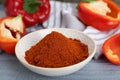 Bowl with aromatic paprika powder and fresh bell peppers on grey wooden table, closeup Royalty Free Stock Photo