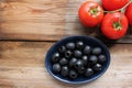 Bowl of black olives and fresh tomatoes on the vine on rustic wooden table background. Pasta or salad ingredients. Royalty Free Stock Photo