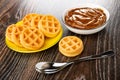 Bowl with boiled condensed milk, soft waffles in yellow saucer, spoon and waffle on wooden table Royalty Free Stock Photo