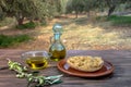 Bowl and bottle with extra virgin olive oil, olives, a fresh branch of olive tree and cretan rusk dakos on wooden table.