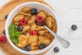 Bowl for breakfast with tiny pancake cereal with blueberries, raspberries, mint