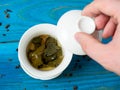 A bowl of brewed tea on a blue wooden background. A hand lifts the lid of the bowl. The opened leaves of large-leaved tea. Chinese