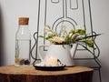 A bowl with a burning candle decorated with white pebbles, glass bottle with water and cork and next to it a teapot with floral