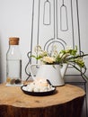 A bowl with a burning candle decorated with white pebbles, glass bottle with water and cork and next to it a teapot with floral