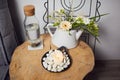 A bowl with a burning candle decorated with white pebbles, glass bottle with water and cork and next to it a teapot with floral