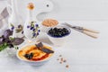 A bowl of chickpeas homemade hummus with olive oil, basil, black olives and smoked paprika on white wooden background