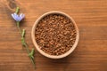 Bowl of chicory granules and flower on wooden table, flat lay