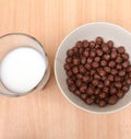 Bowl with chocolate balls and a cup of milk on a wooden table. Sweet cocoa, chocolate, sugar, cereal, puffs with milk