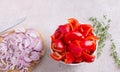 A bowl of chopped red sweet peppers, a wooden board with chopped red onions, fresh thyme sprigs and a kitchen knife on a Royalty Free Stock Photo