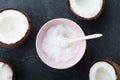 Bowl with coconut oil and fresh half of coconuts on black stone table top view. Beauty and spa homemade cosmetic. Flat lay. Royalty Free Stock Photo